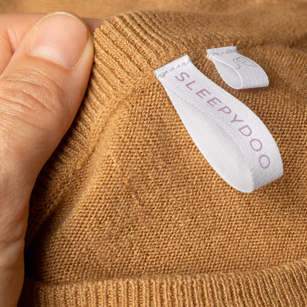 Close-up of a hand holding a brown knit garment with a white label reading 'SLEEPYDOO'.