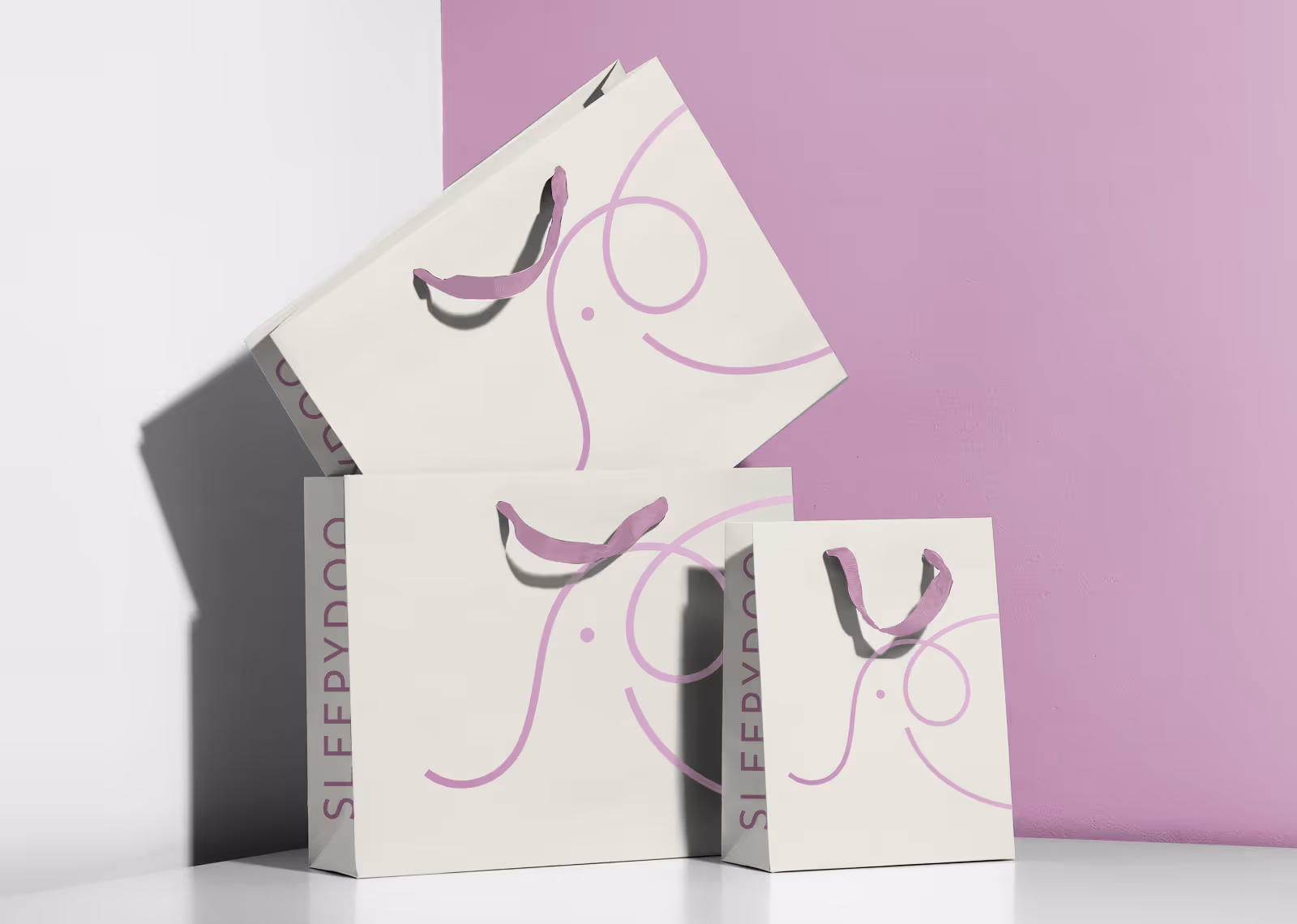 Three cream-colored shopping bags with purple ribbon handles and a minimalist purple elephant design stacked against a white and purple wall.