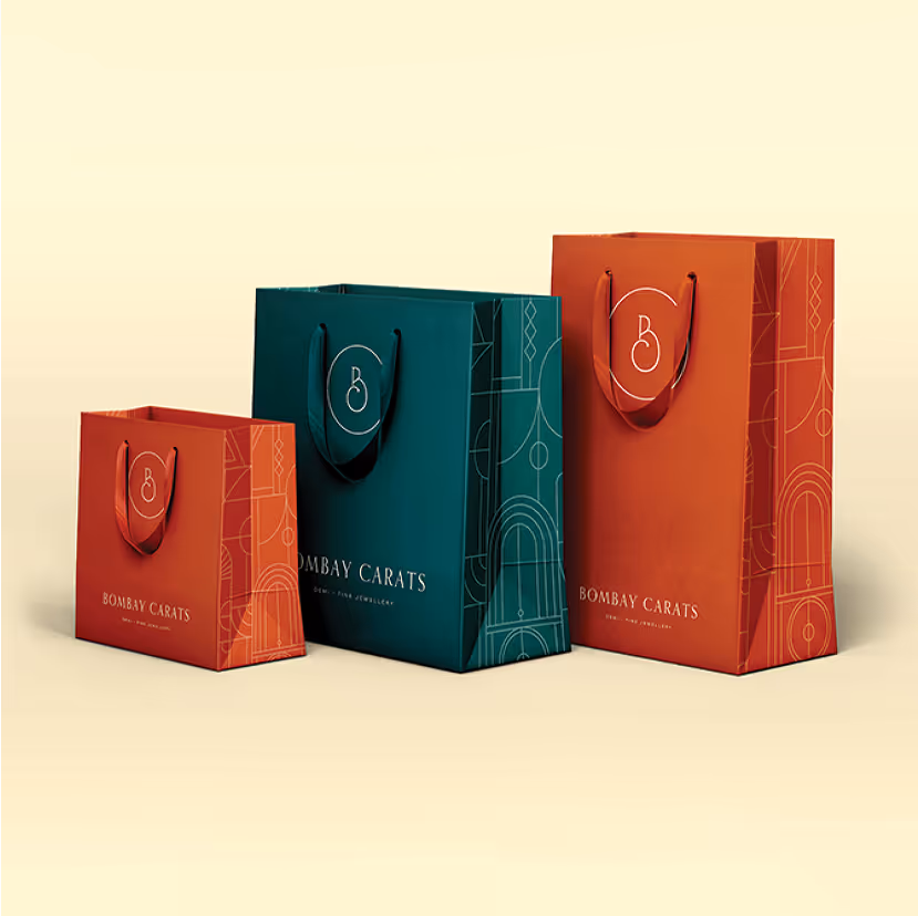 Three Bombay Carats branded shopping bags in varying sizes with geometric designs on a light beige background.