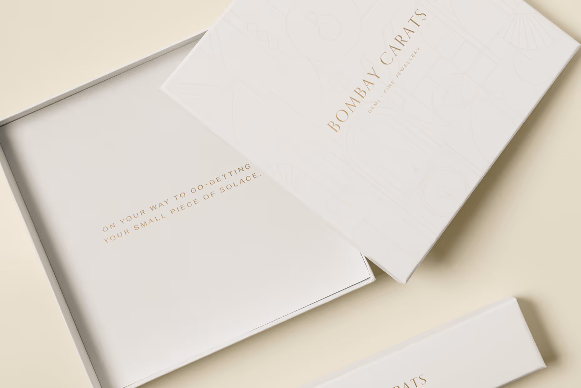 Partially open white luxury jewelry box with 'BOMBAY CARATS' branding and gold text inside saying 'On your way to go-getting your small piece of solace.'