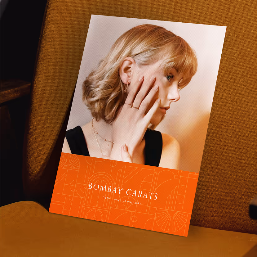Printed ad featuring a woman with short blonde hair showcasing delicate jewelry, with the text "Bombay Carats Demi Fine Jewellery" on an orange geometric background.