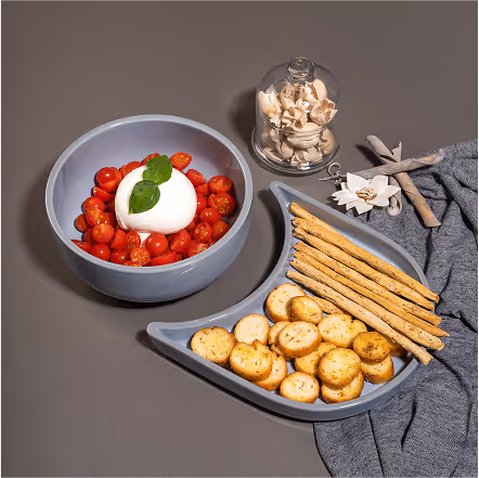 Bowl of cherry tomatoes topped with mozzarella cheese and basil, accompanied by breadsticks and round garlic crackers on a triangular plate.