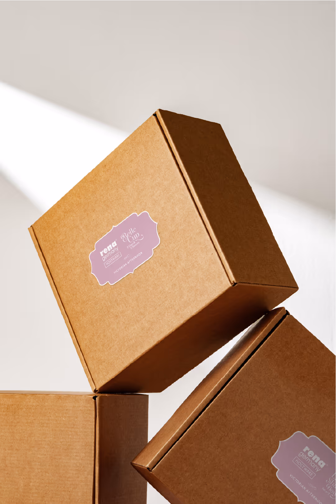 Three brown cardboard boxes stacked together, each with a purple label reading 'rena germany frostware Belle Cup Victorian Afternoon'.