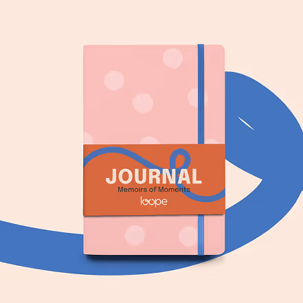 Pink journal with light pink polka dots and a blue elastic band, labeled 'JOURNAL Memoirs of Moments' on an orange band.