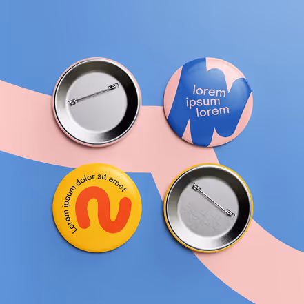 Four round pin-back buttons on blue and pink surface: two with text and abstract design, two showing metal backs.