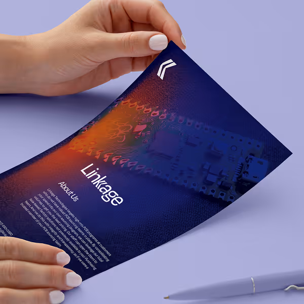 Hands holding a printed brochure titled 'Linkage' with a circuit board image and a pen on a lavender surface.