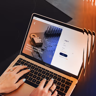 Person typing on a MacBook Air laptop displaying a login screen and an image with the text 'Walking with you at every step in the process.'