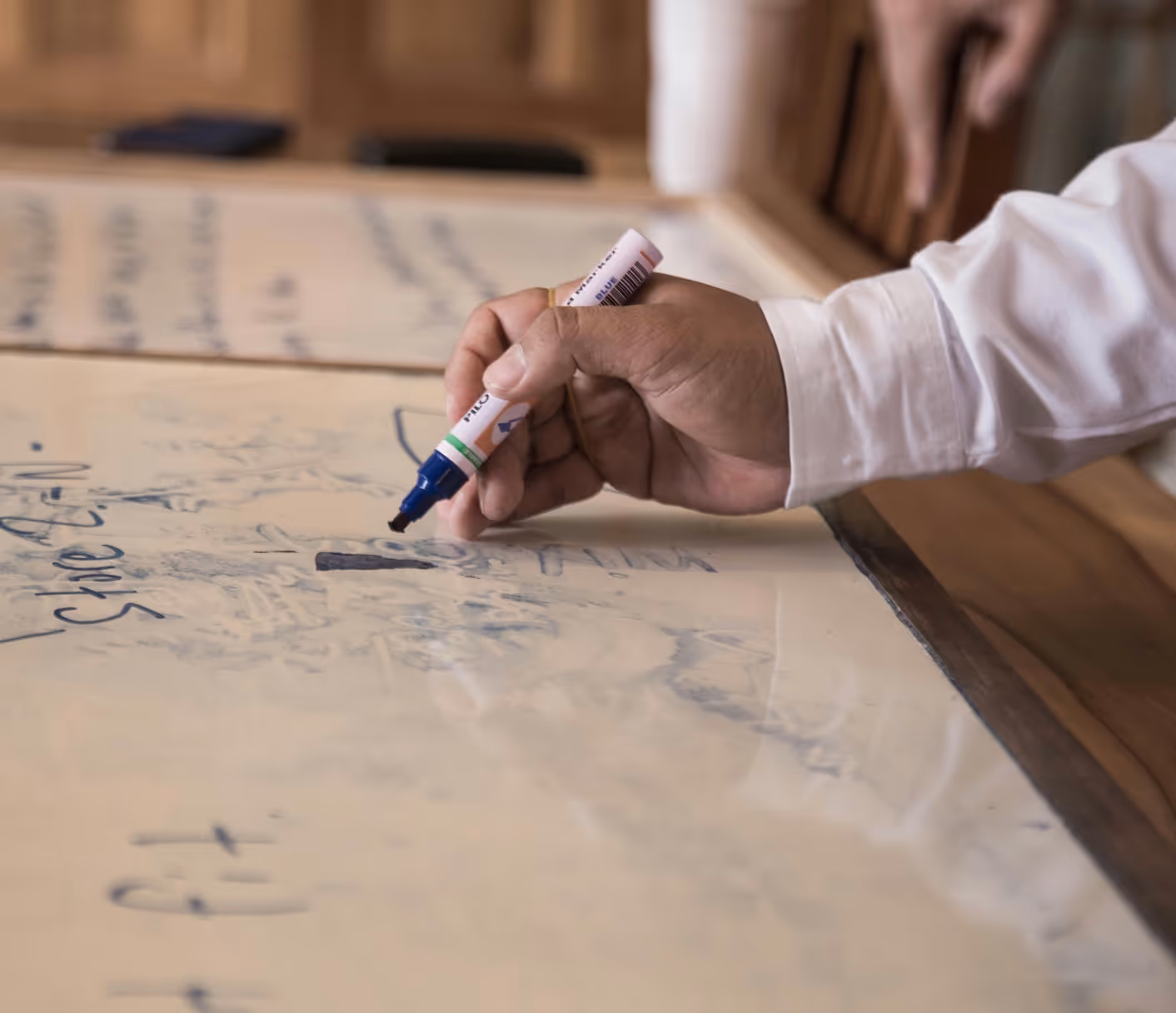 A hand holding a blue marker writing on a large sheet of paper with handwritten notes.