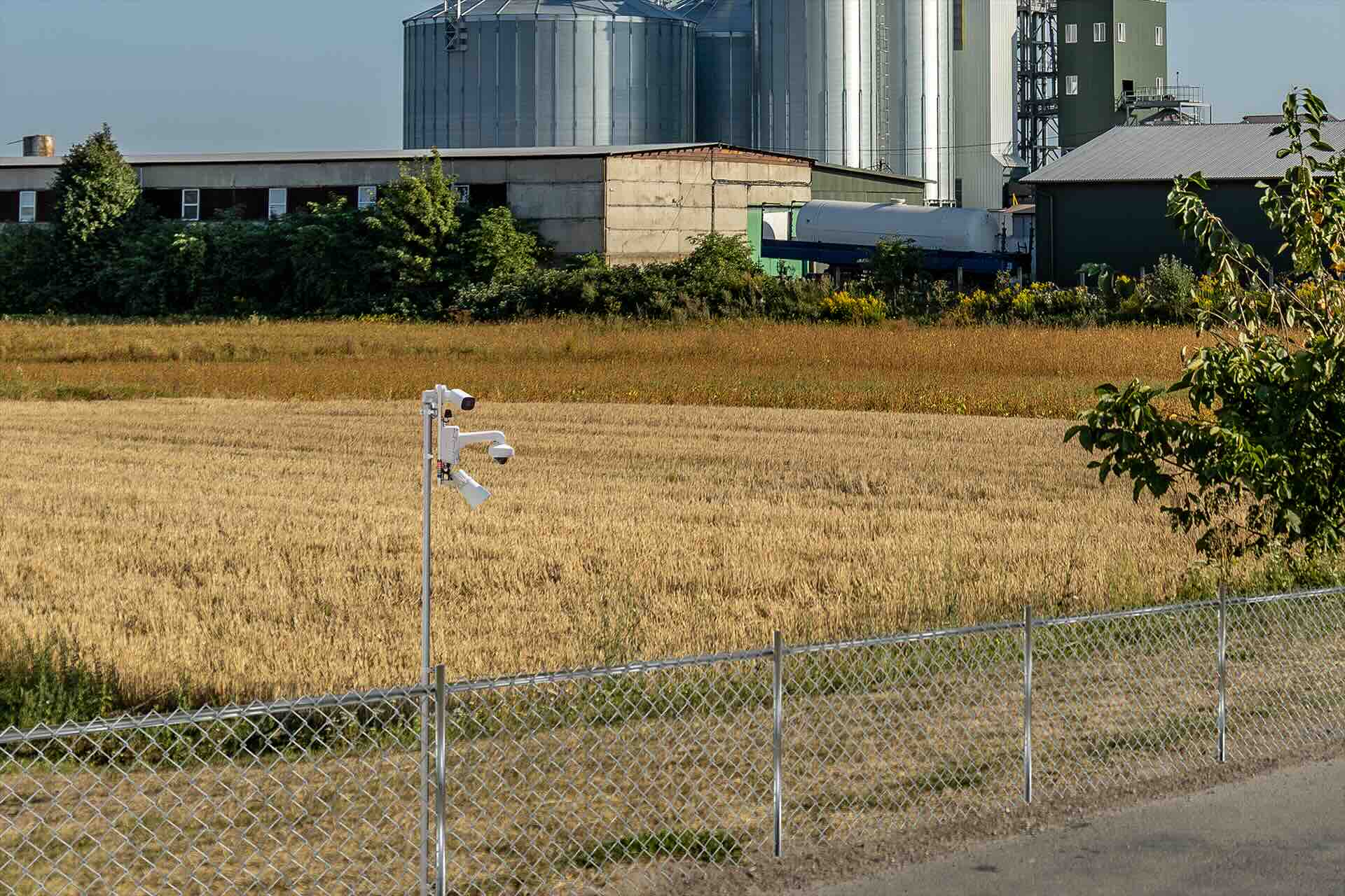SmartGuard mounted on a pole with security cameras and alert light overlooking fenced wheat field with grain facility in the distance. 