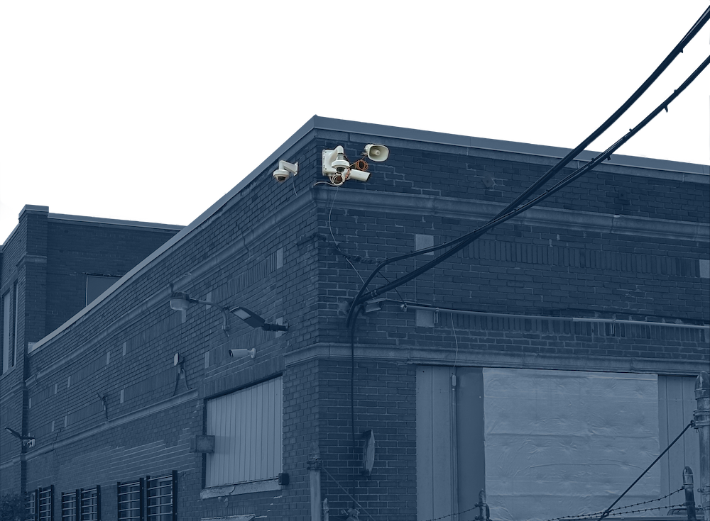Exterior corner of a brick building with SmartGuard unit including cameras and a loudspeaker attached near the roof.