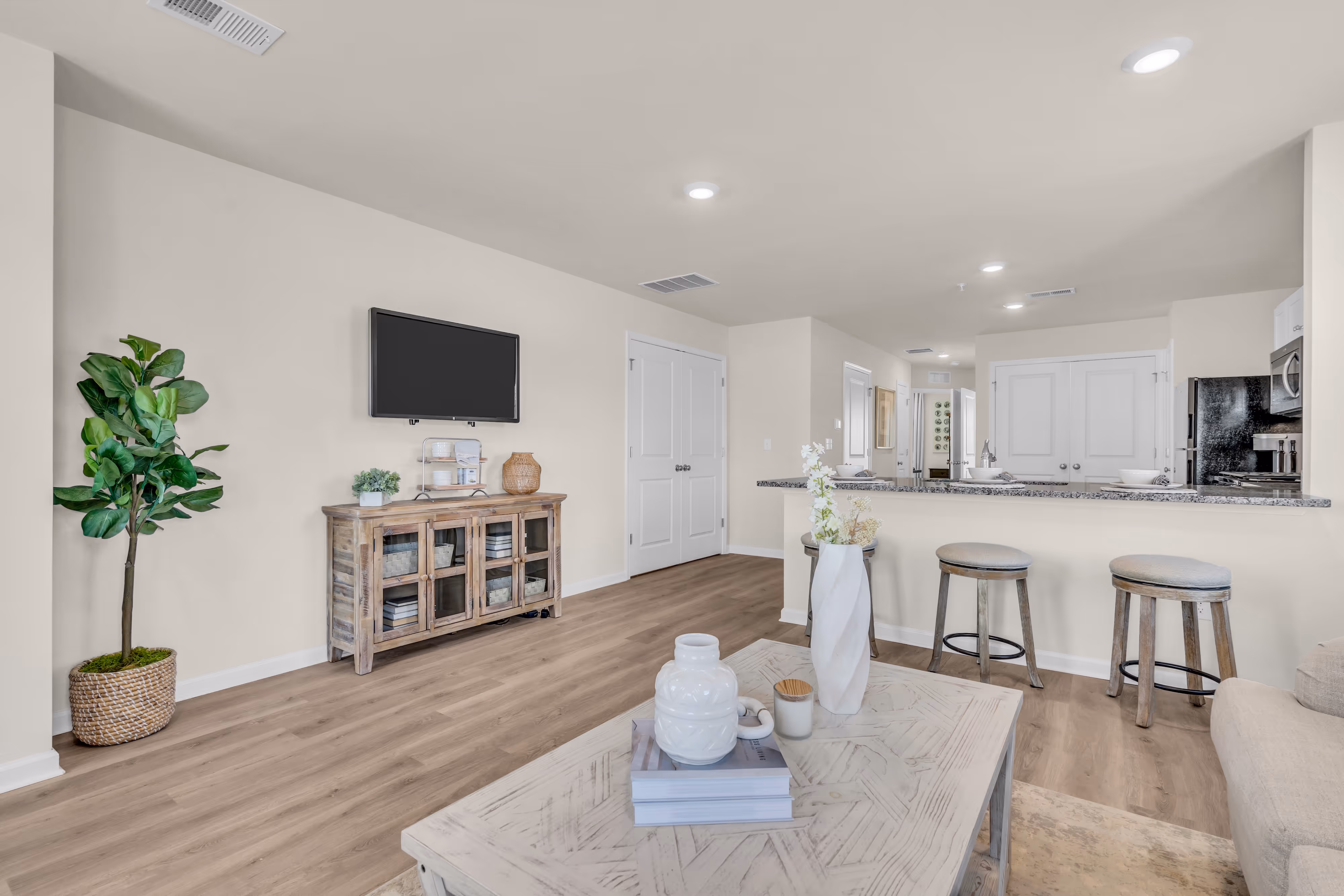 Spacious living room with a TV console, plant, and bar seating leading to the kitchen, in an apartment at Rancocas Pointe in Burlington Township, NJ.