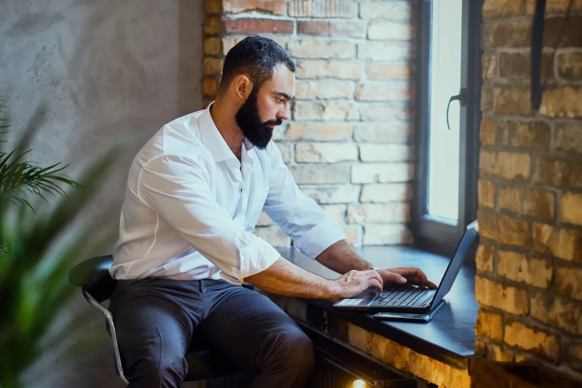 Stylish bearded male works with laptop