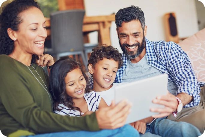 Photograph of a smiling family sitting together and looking at a tablet screen.