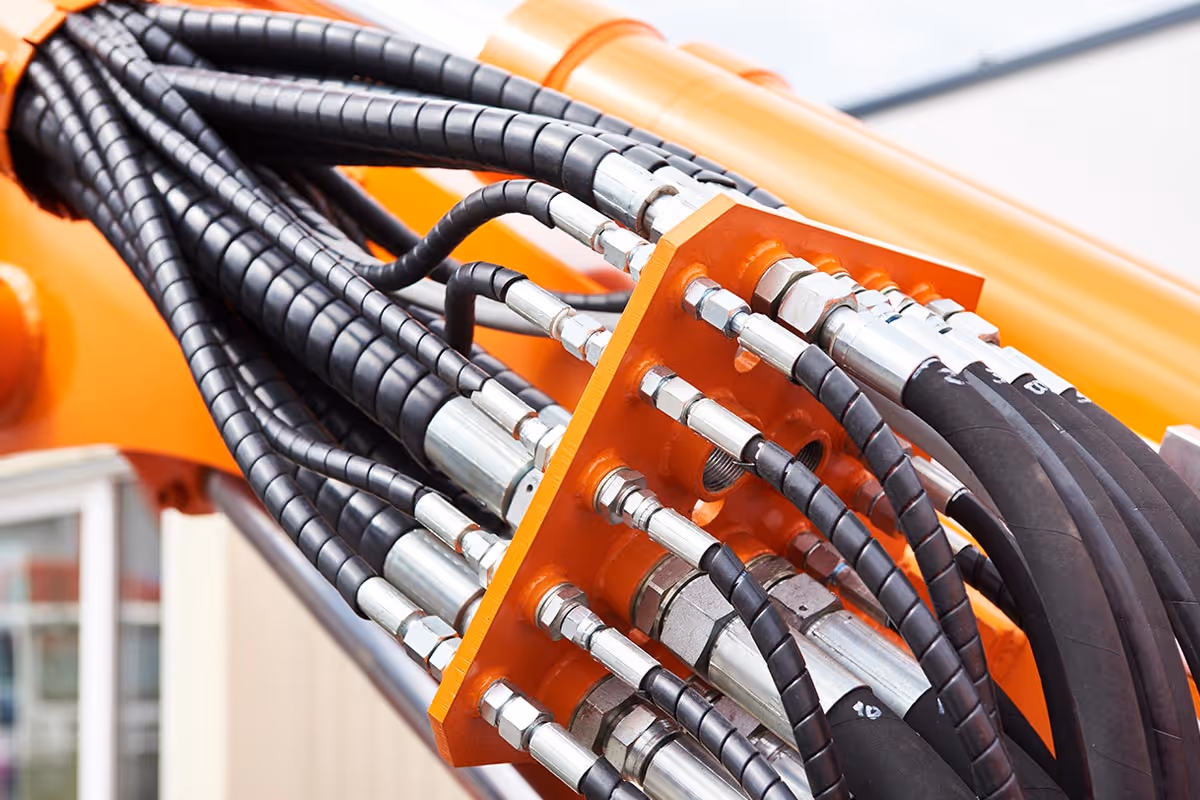 Hydraulikschläuche und Verschraubungen an orangefarbener Baumaschine