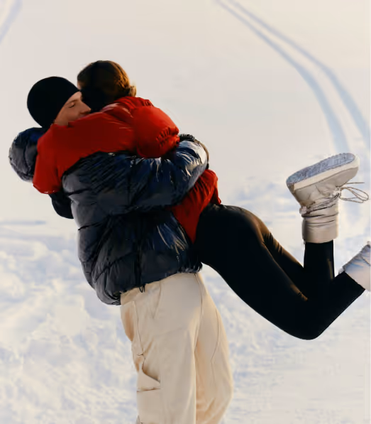 Couple dressed in winter clothes hugging and smiling outdoors in the snow.