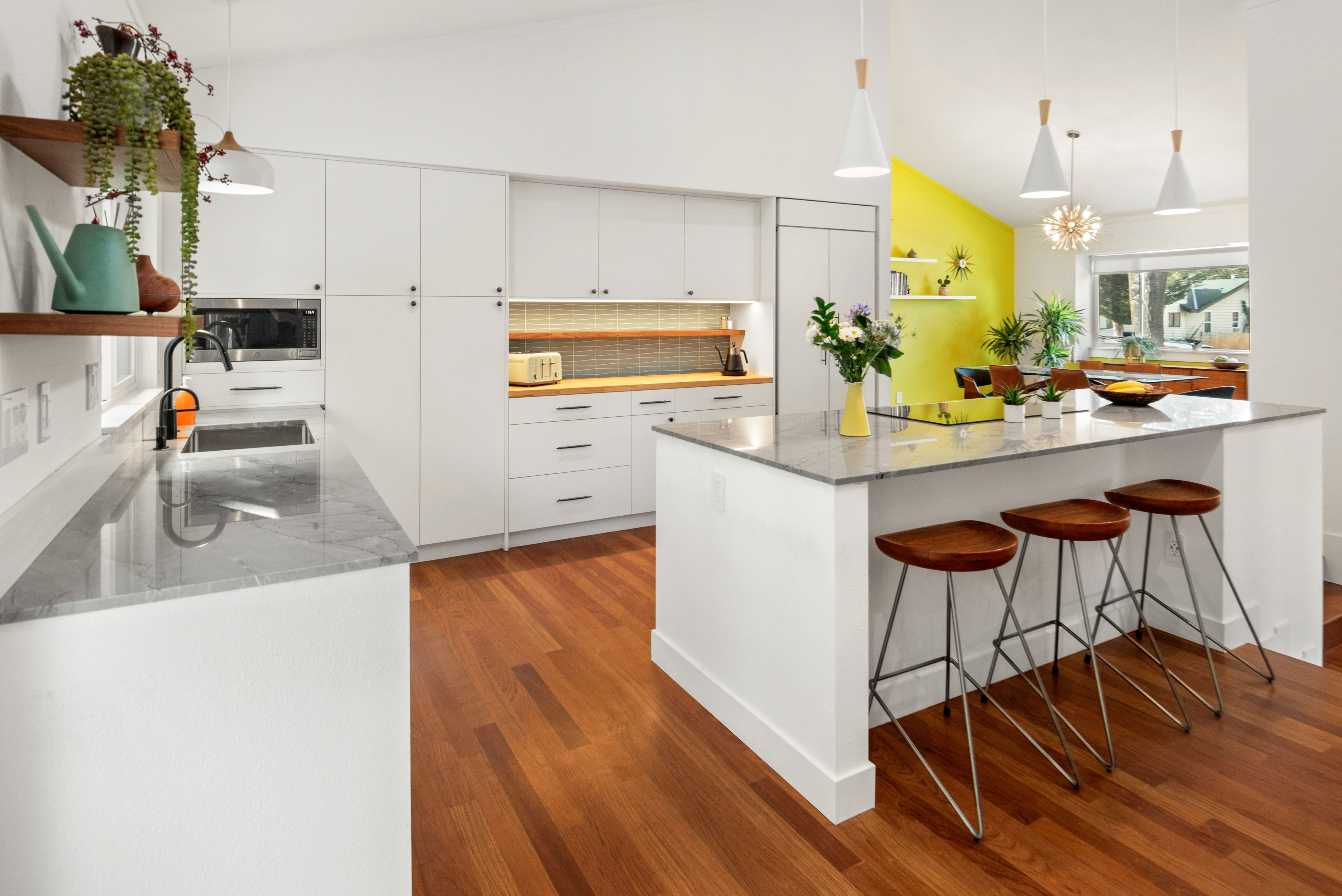 Mid-century kitchen with white cabinetry, a stone island and wood floors