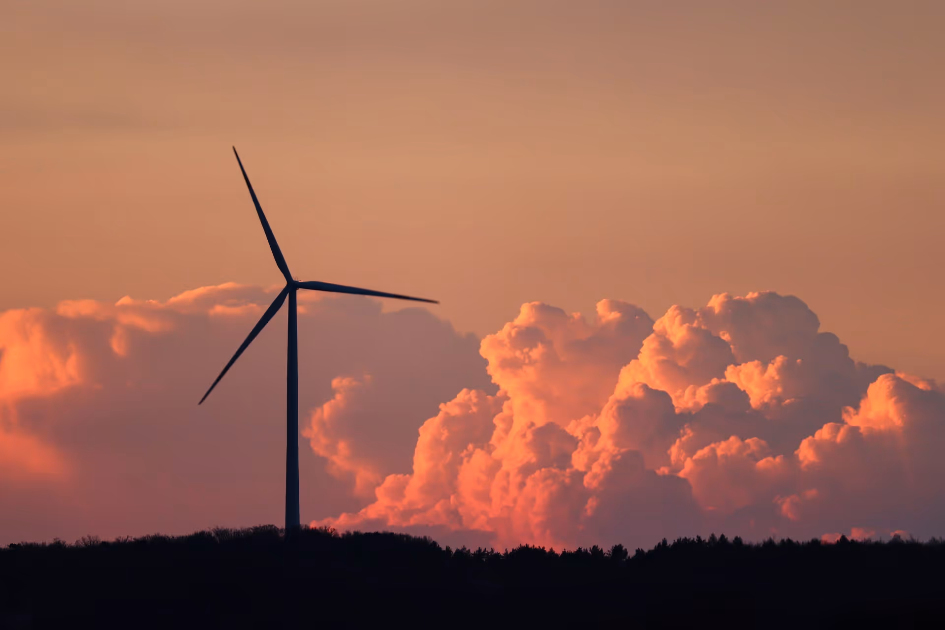 Silhouette of a wind turbine against a background of large, orange sunset clouds.