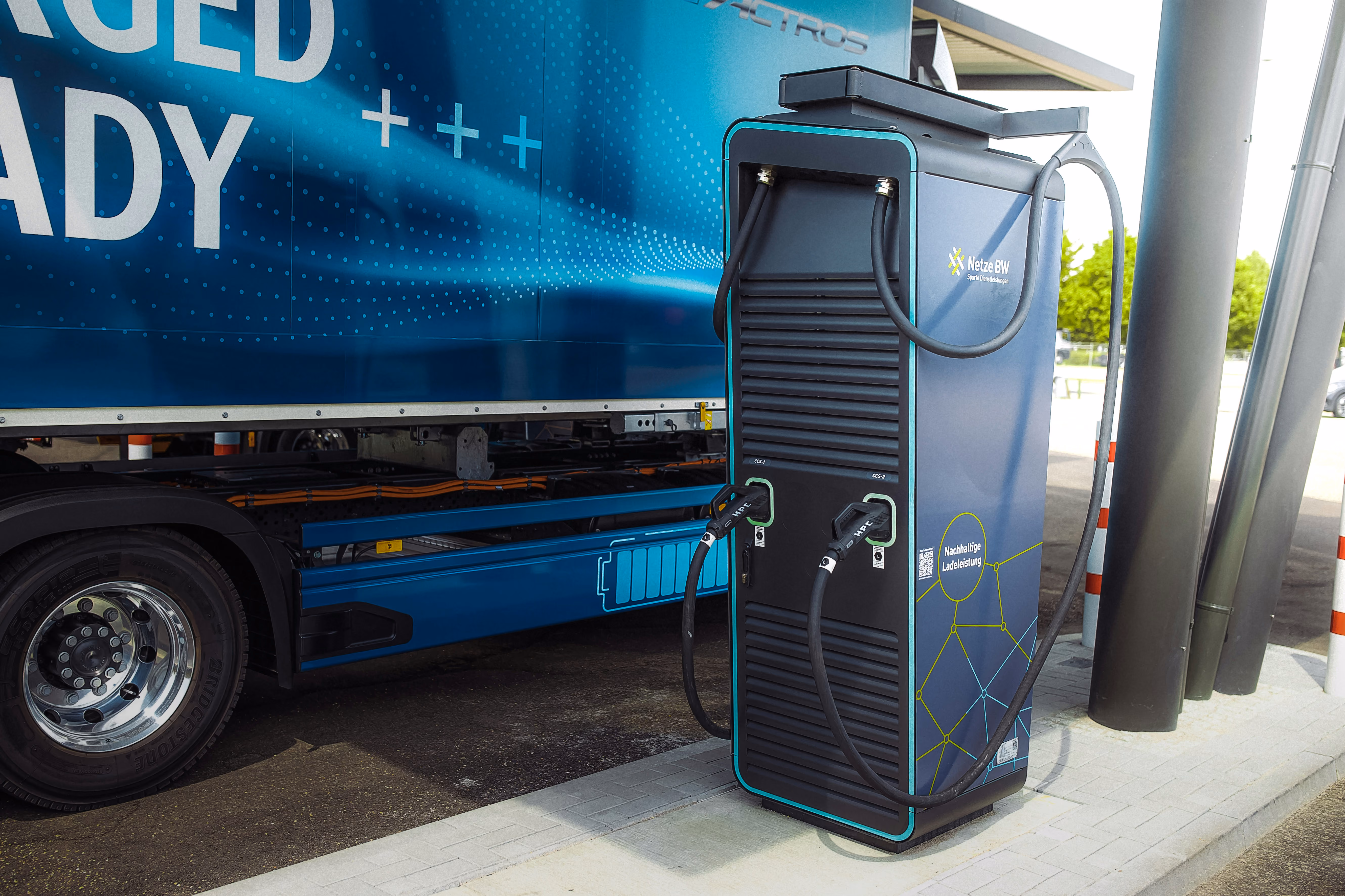 Electric vehicle charging station with two connected cables beside a blue truck.