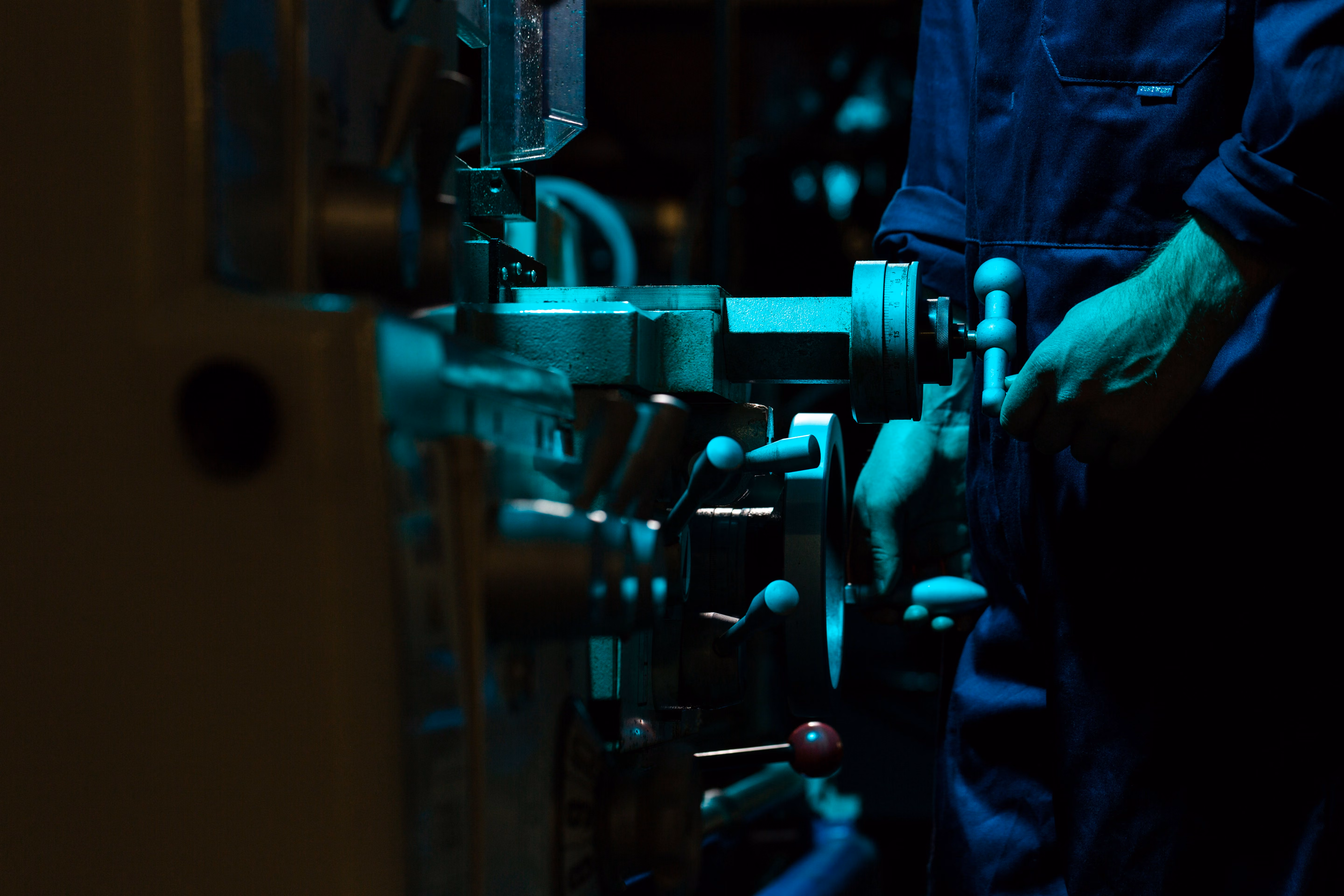 Worker operating a metal lathe machine in a dimly lit industrial setting.
