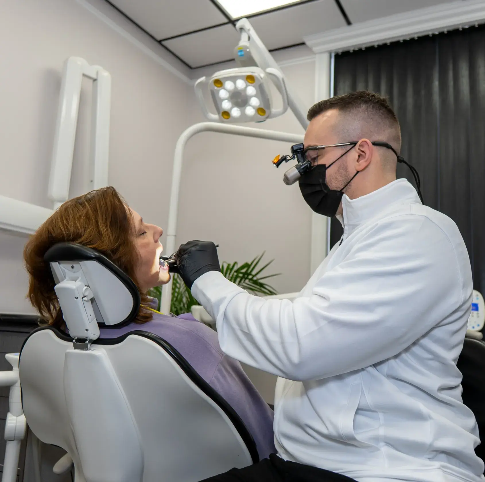 Dentist wearing a mask examines a patient's teeth in a dental office.