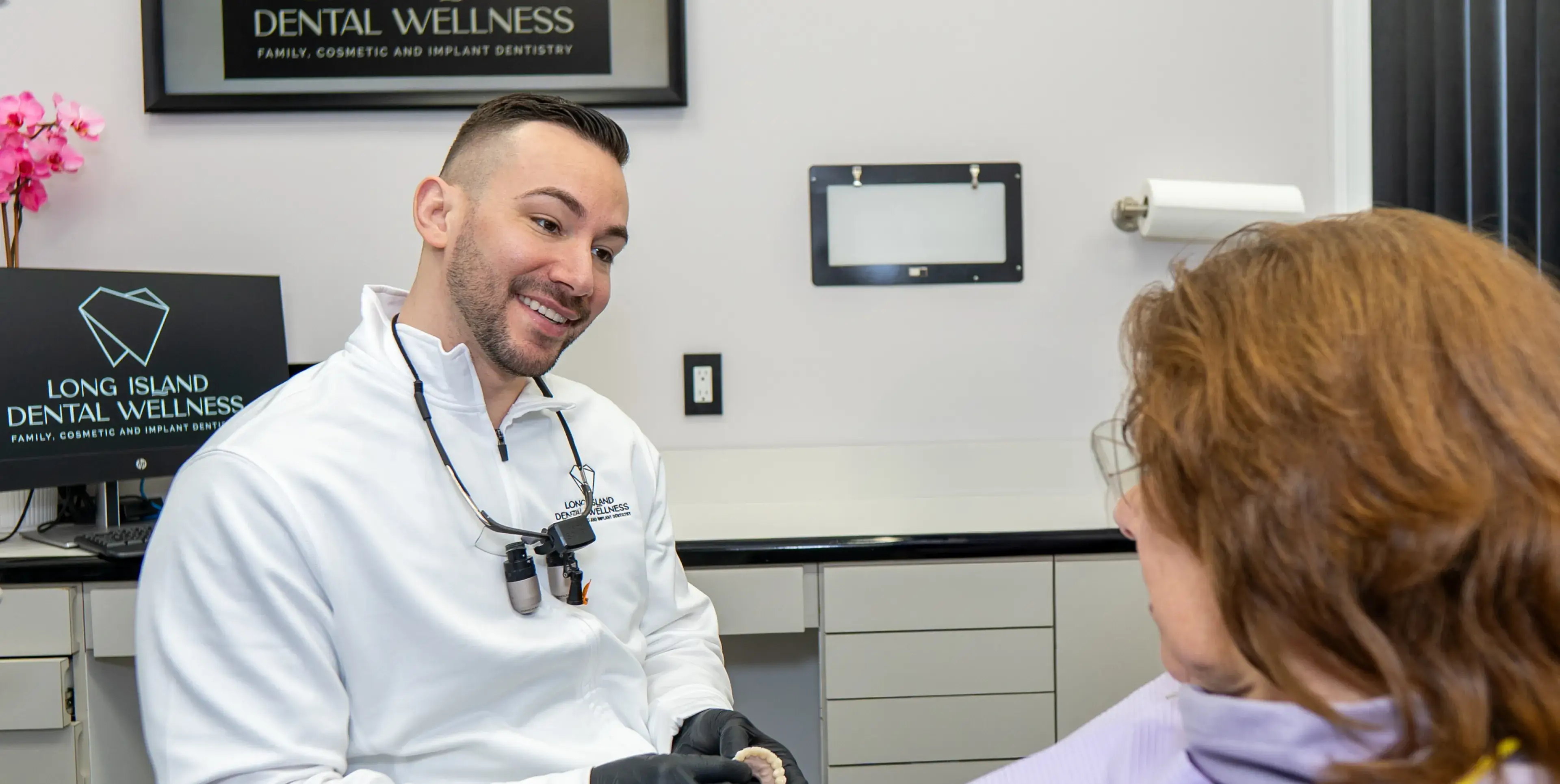 A dentist in a white coat discusses treatment with a patient in the dental office.