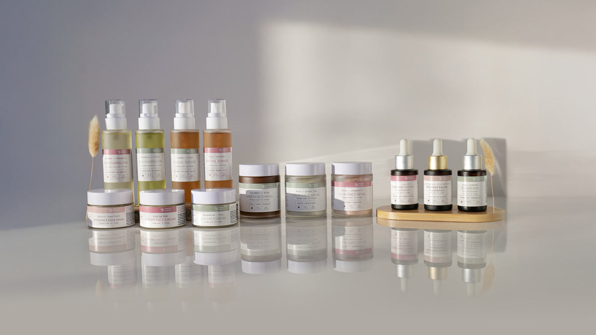 Array of natural skincare products including cleansers, toners, creams, face masks, and serums on a reflective surface.