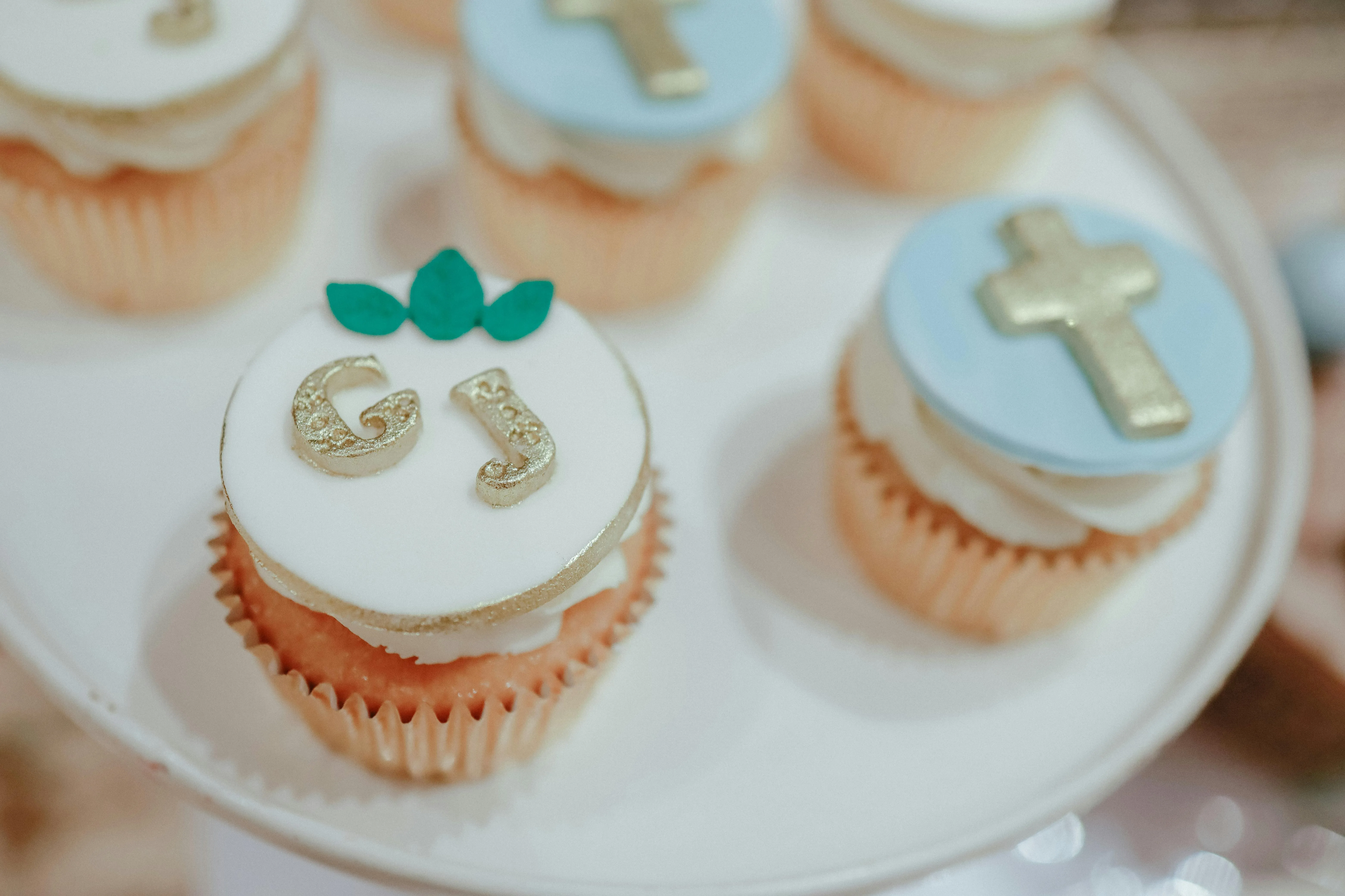 Tauf-Cupcakes mit weißem Zuckerguss, Goldperlen und Kreuzsymbol – elegant arrangiert für die Festtafel von Babybloom Wien