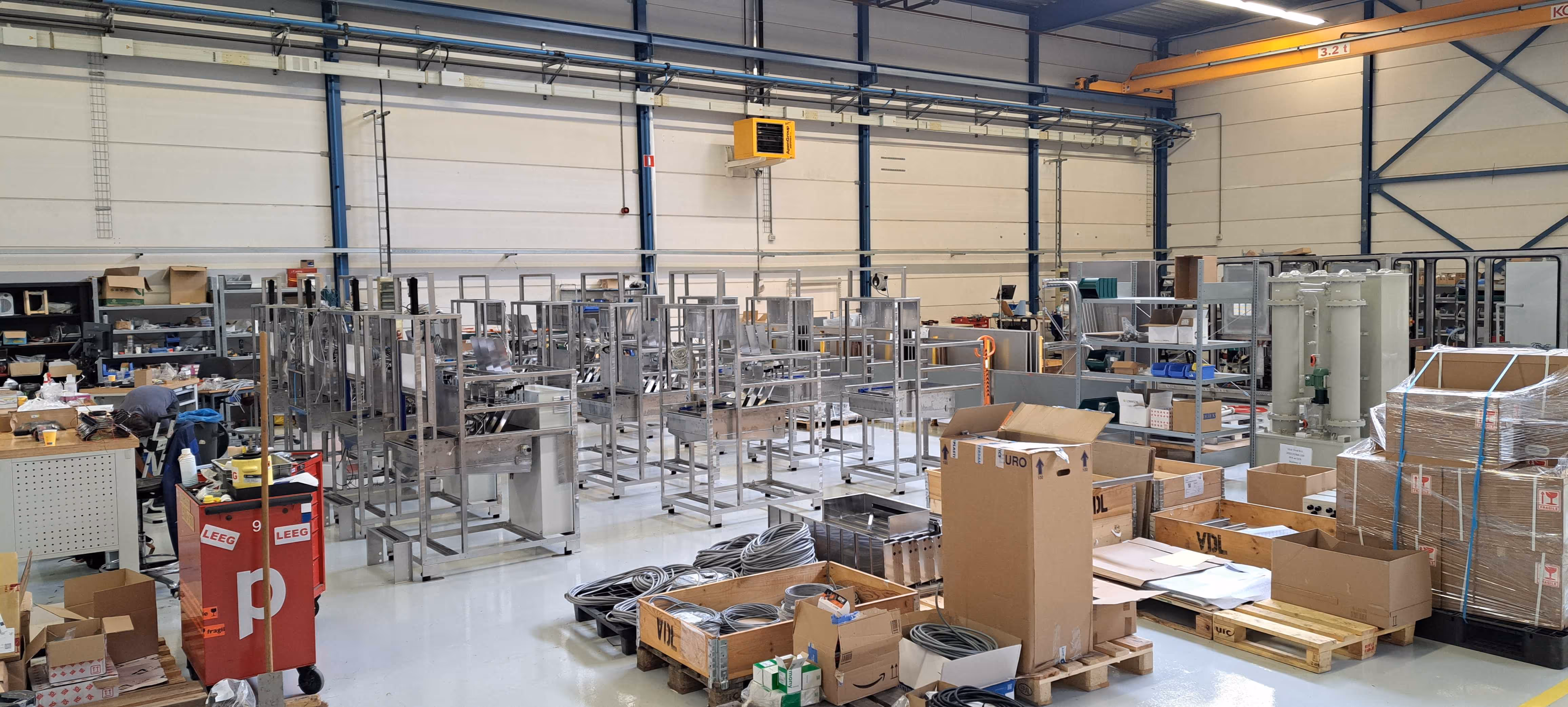 Grootschalige werkplaats met metalen frames, dozen en technische uitrusting op pallets.