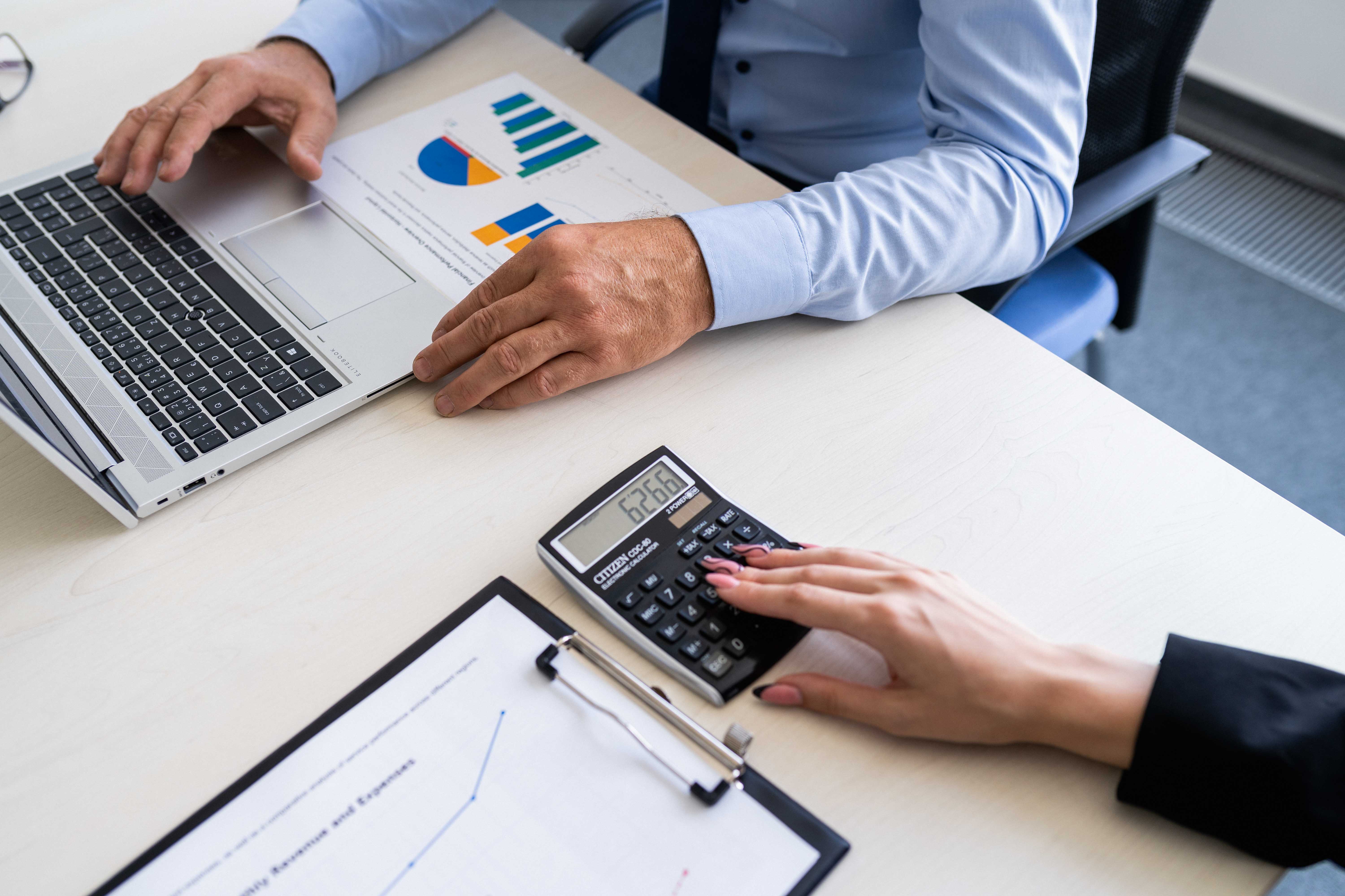Two people sitting at a table with a calculator and a laptop