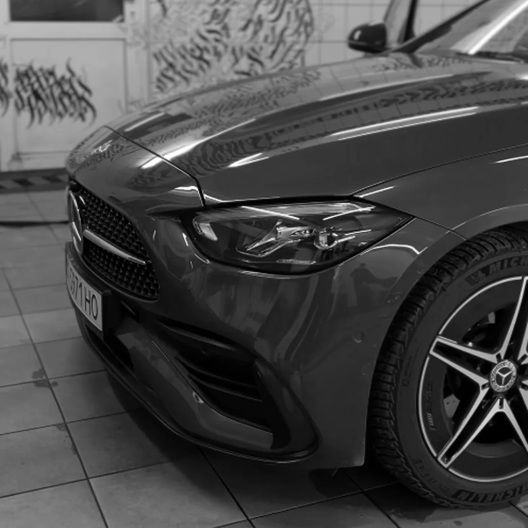 Передня частина чорного Mercedes-Benz із блискучим капотом та сучасною фариною у гаражі.