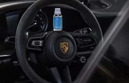 Пляшка синьої рідини для салону, закріплена на кермі Porsche у салоні автомобіля.