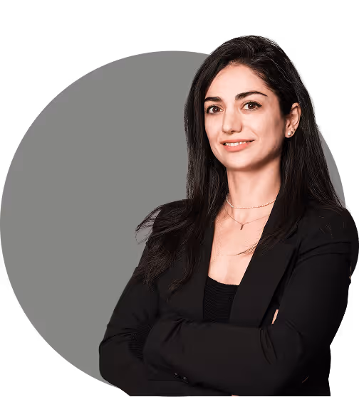 Eine Frau in einem schwarzen Blazer steht selbstbewusst mit verschränkten Armen vor einem sanften grauen kreisförmigen Hintergrund.