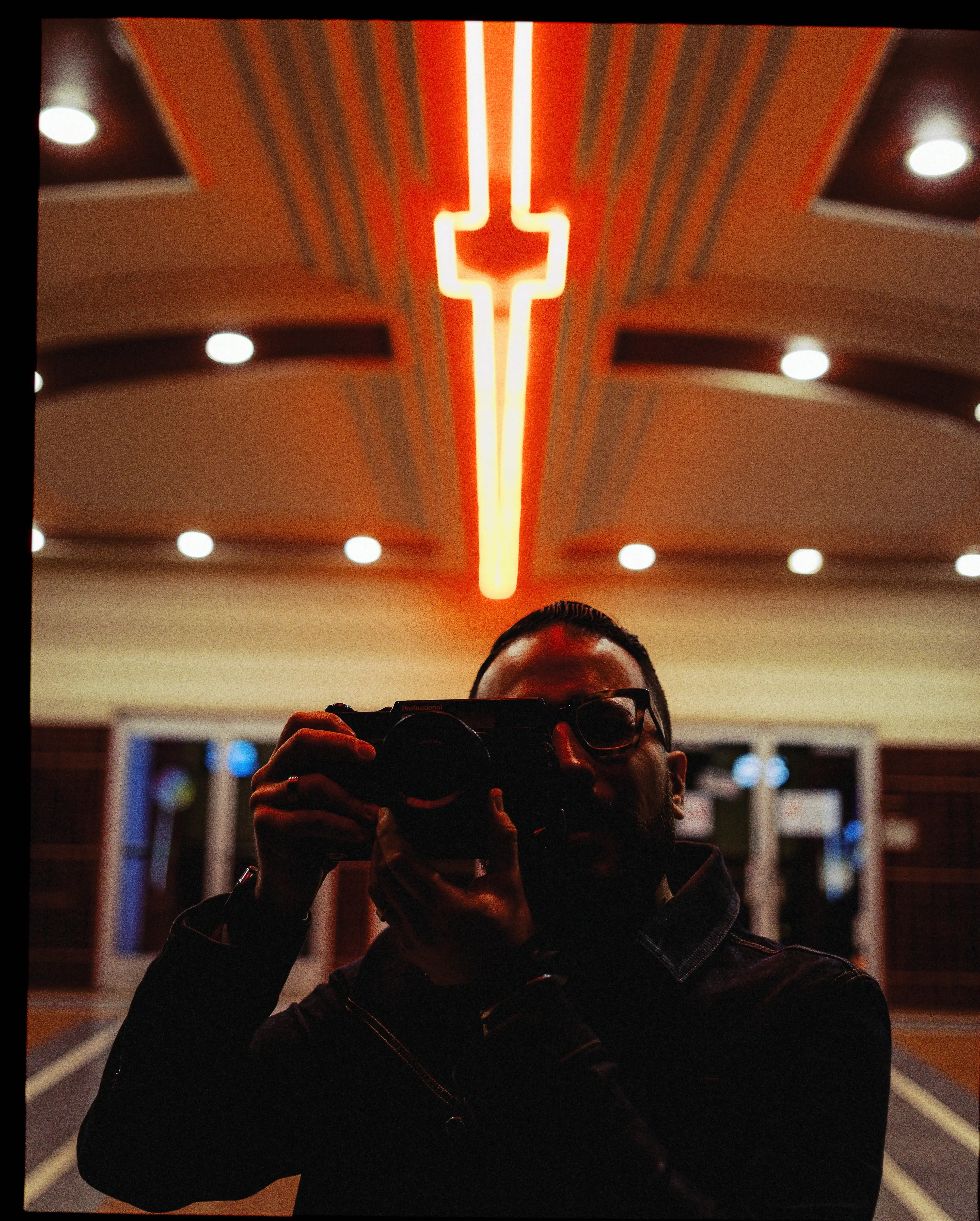 a Photographer holding a Fujifilm Medium Format Camera at night, photographing a neon personal project.