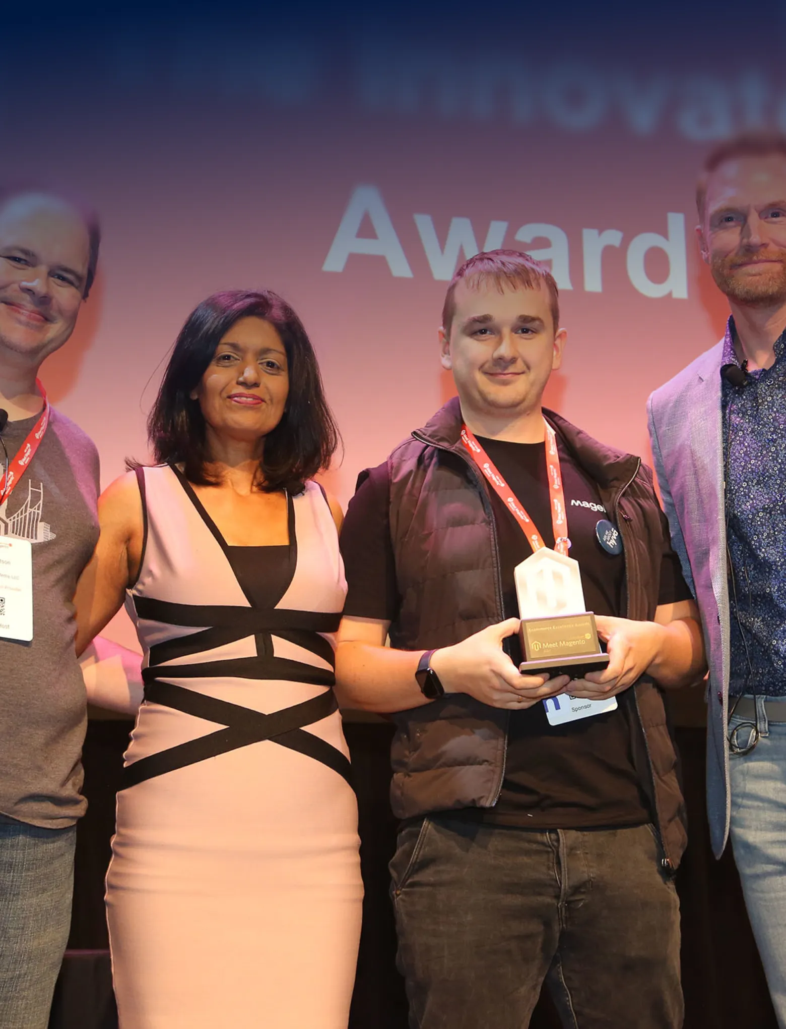 Group photo of four people at an awards event, one holding a trophy with Meet Magento logo.