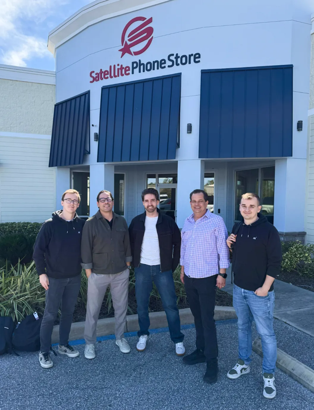 Five men standing outside a building with a Satellite Phone Store sign above the entrance.