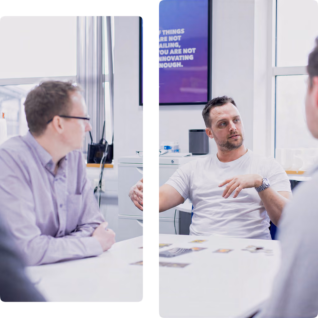 Four men sit in office around white table; one man gestures while speaking, others listen.