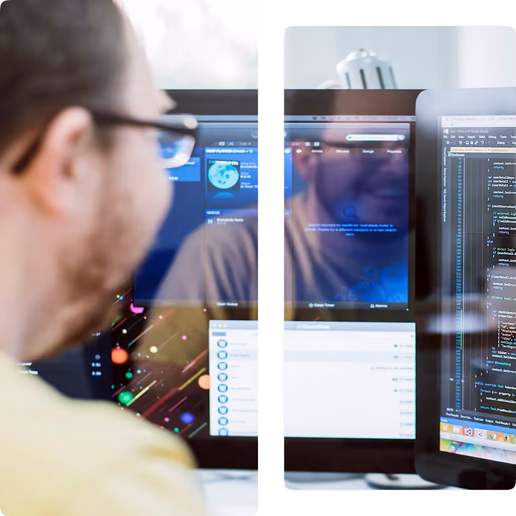 Man wearing glasses sitting at desk viewing two monitors, one showing code and the other a media app.
