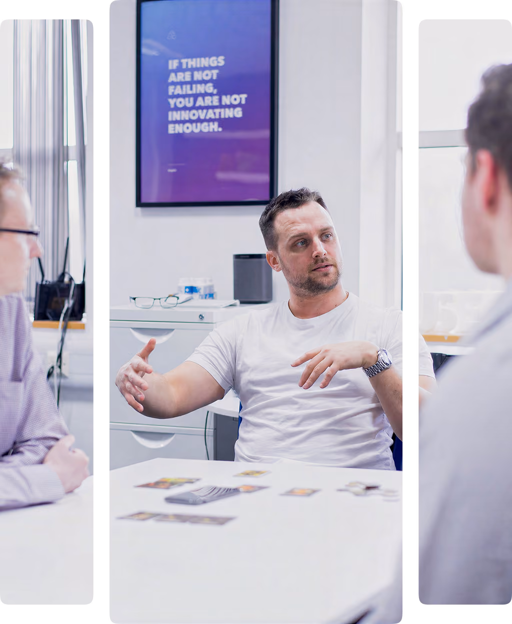 Man in white shirt discussing with two others in a bright office with a motivational poster on the wall.