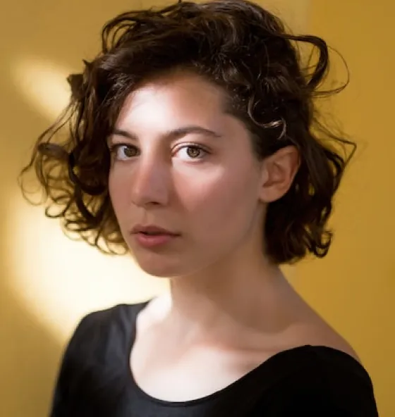 Person with short curly hair wearing a black top against a yellow background.