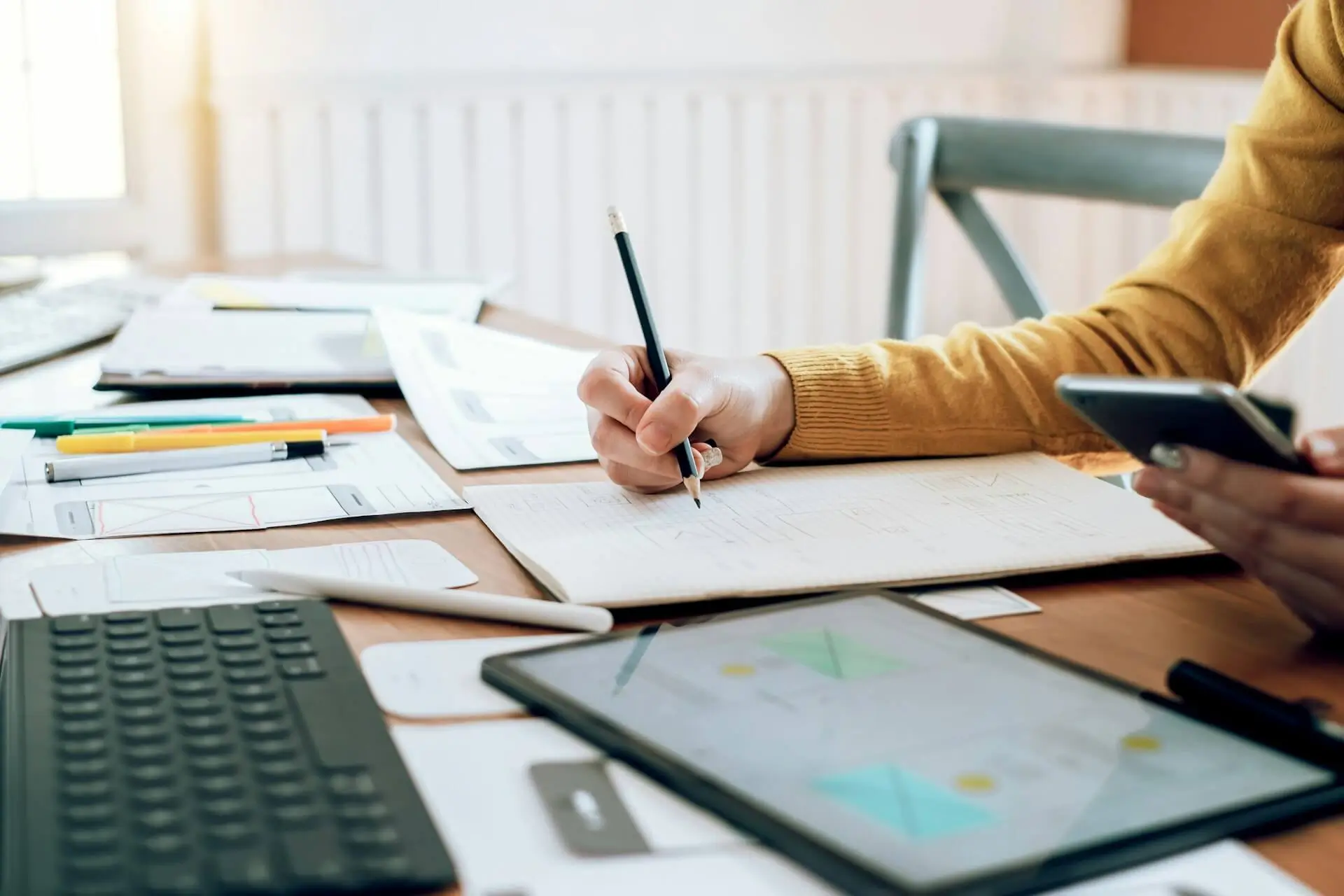 Person planning digital content and GEO strategy at a workspace with notes, mobile device, tablet analytics, and website planning materials
