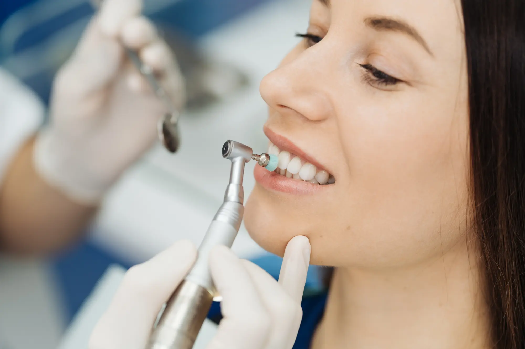 Dentist polishing a woman's teeth with a handheld dental tool