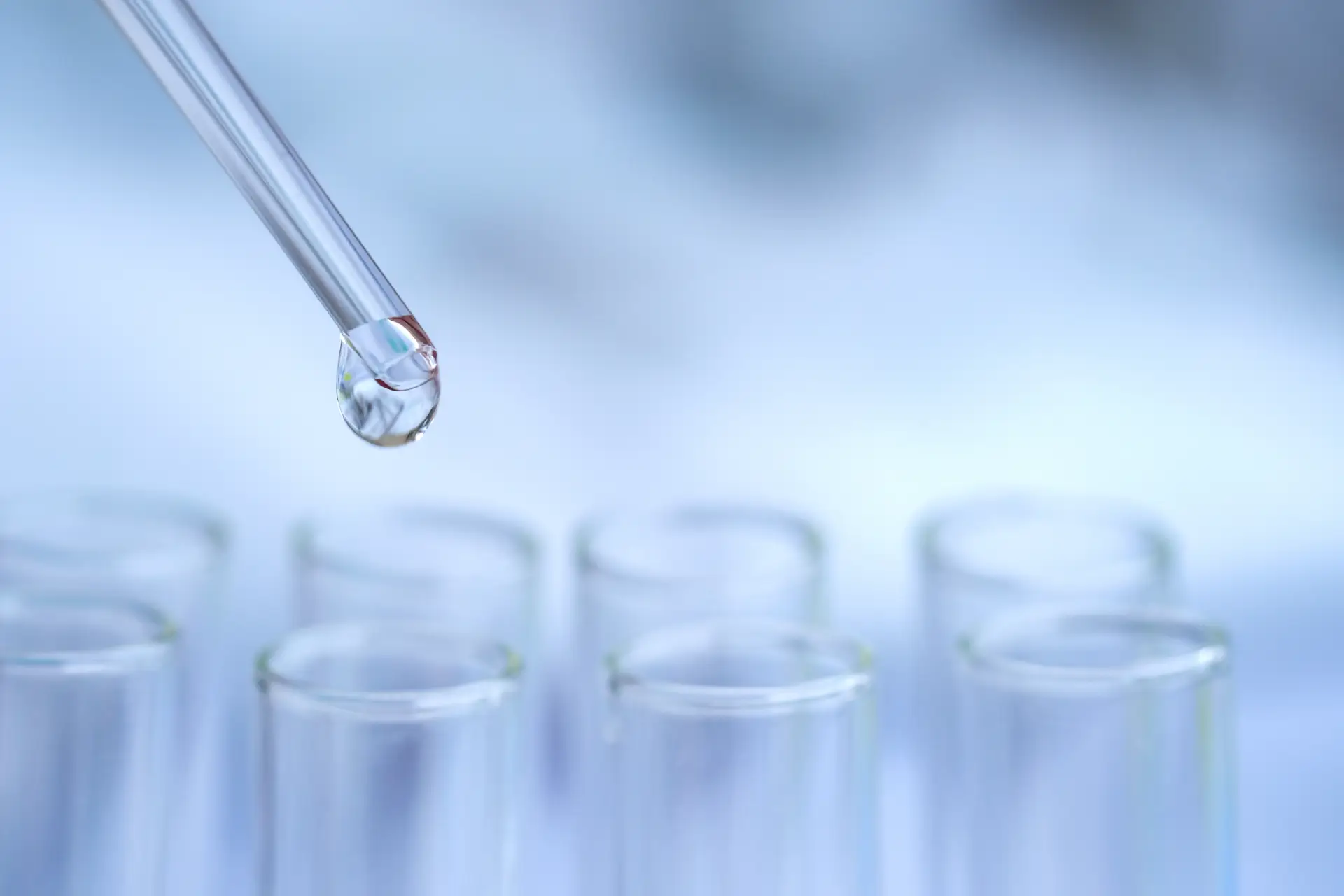 Dropper releasing a liquid droplet above laboratory test tubes