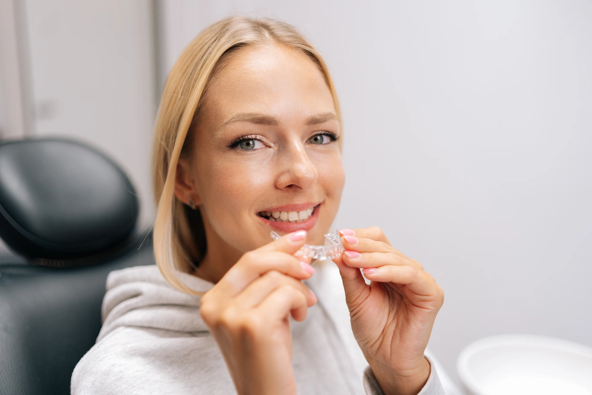 Smiling woman in a dental chair holding a clear aligner