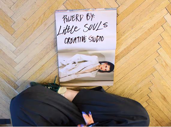 Open magazine on wooden floor showing a woman in white blazer and text 'Powered by Little Souls Creative Studio'.
