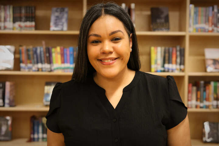 Amy Mendez smiling in front of school library bookshelves