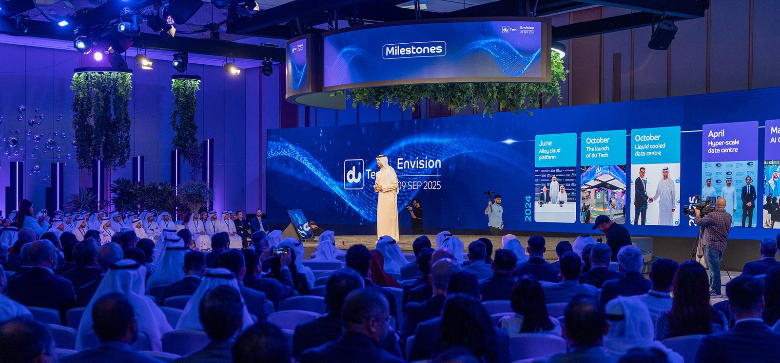 Speaker presenting against an ultra-wide stage display designed for du Tech Envision 2025