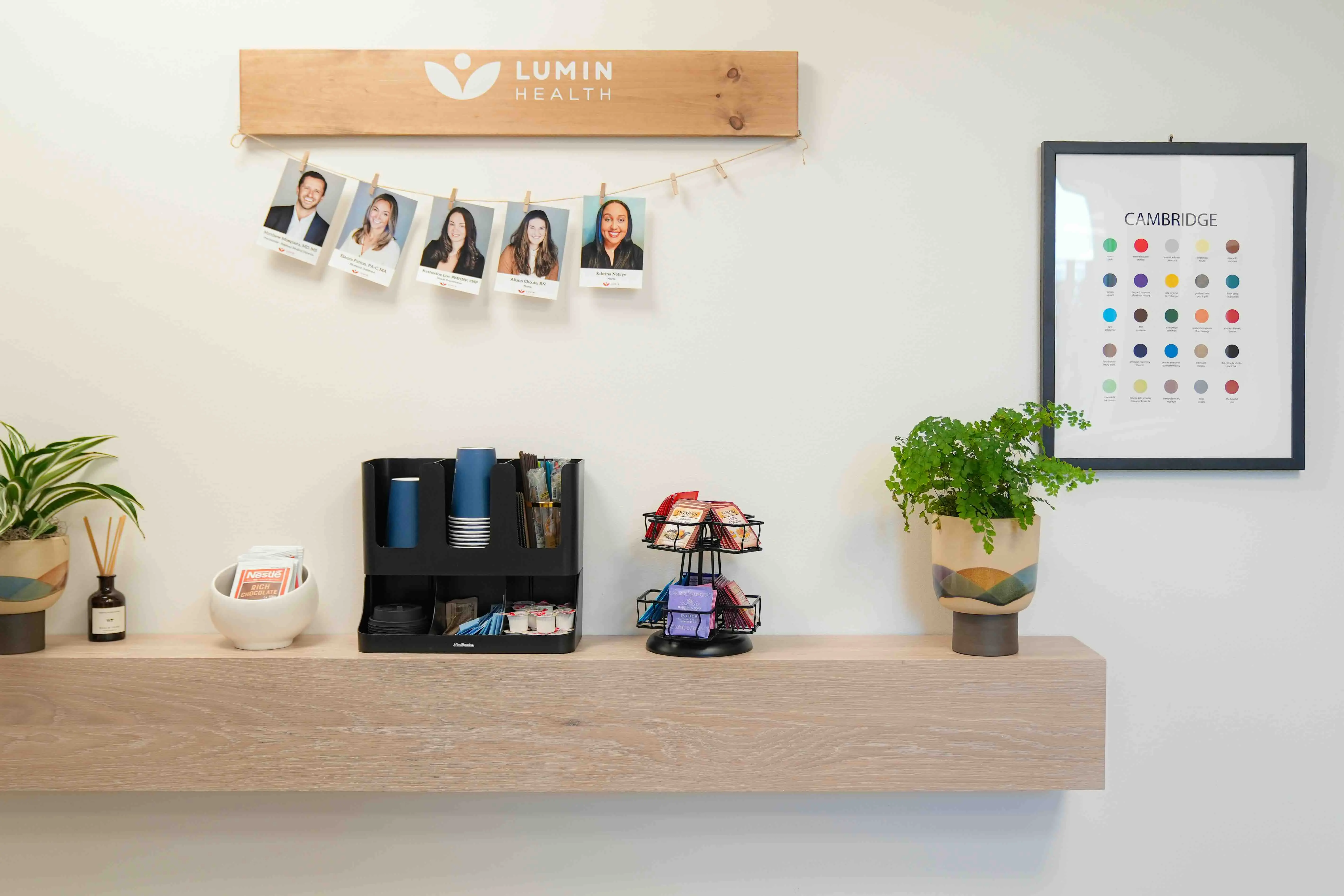 A bright Lumin Health front desk with team photos, a wood shelf, plants, and a framed color chart