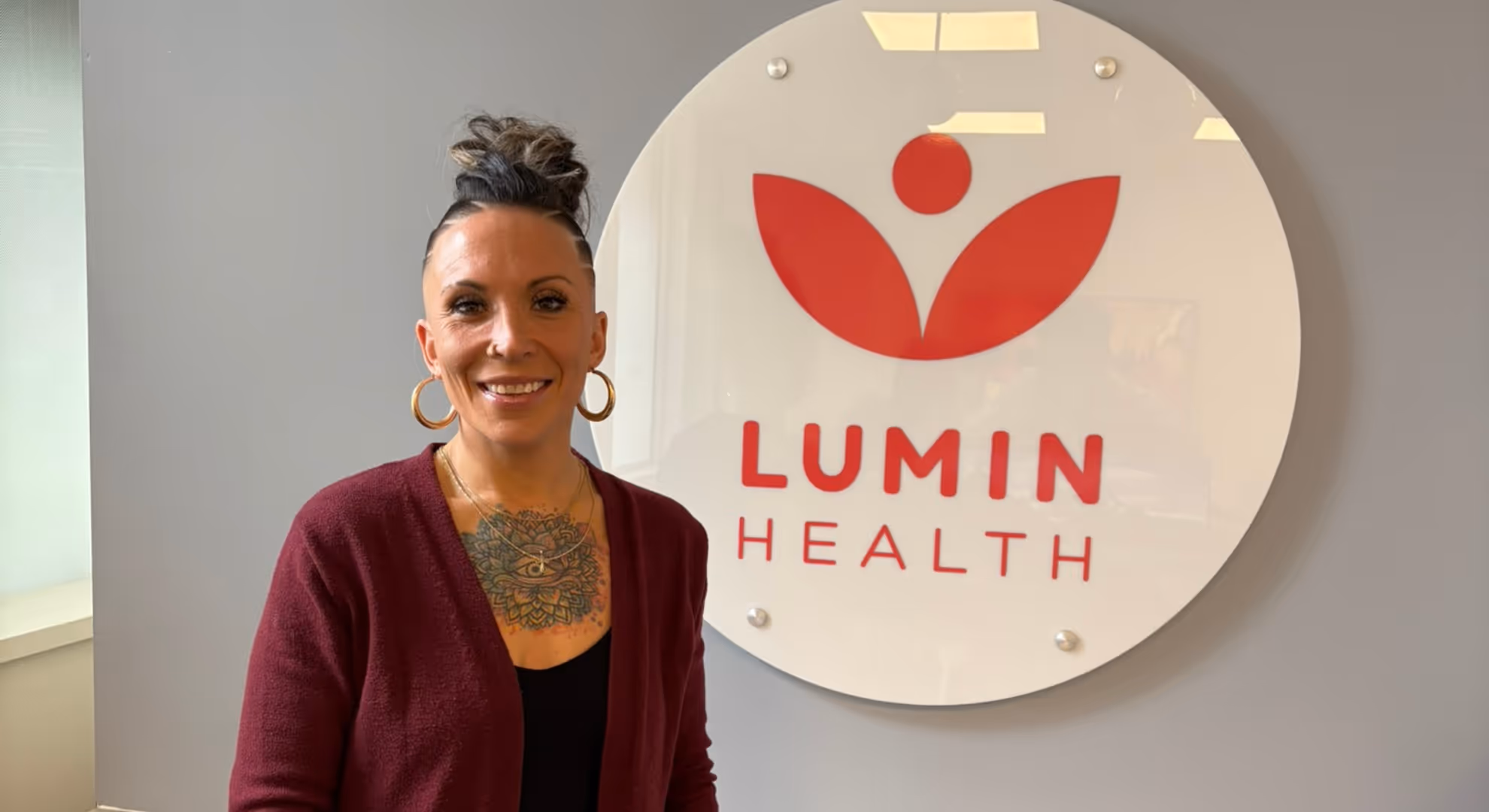 Brittany, a Lumin Health patient, smiling beside the Lumin Health logo at a Lumin Health location.