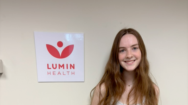 Lila, a Lumin Health patient, smiling beside the Lumin Health logo at a Lumin Health location.