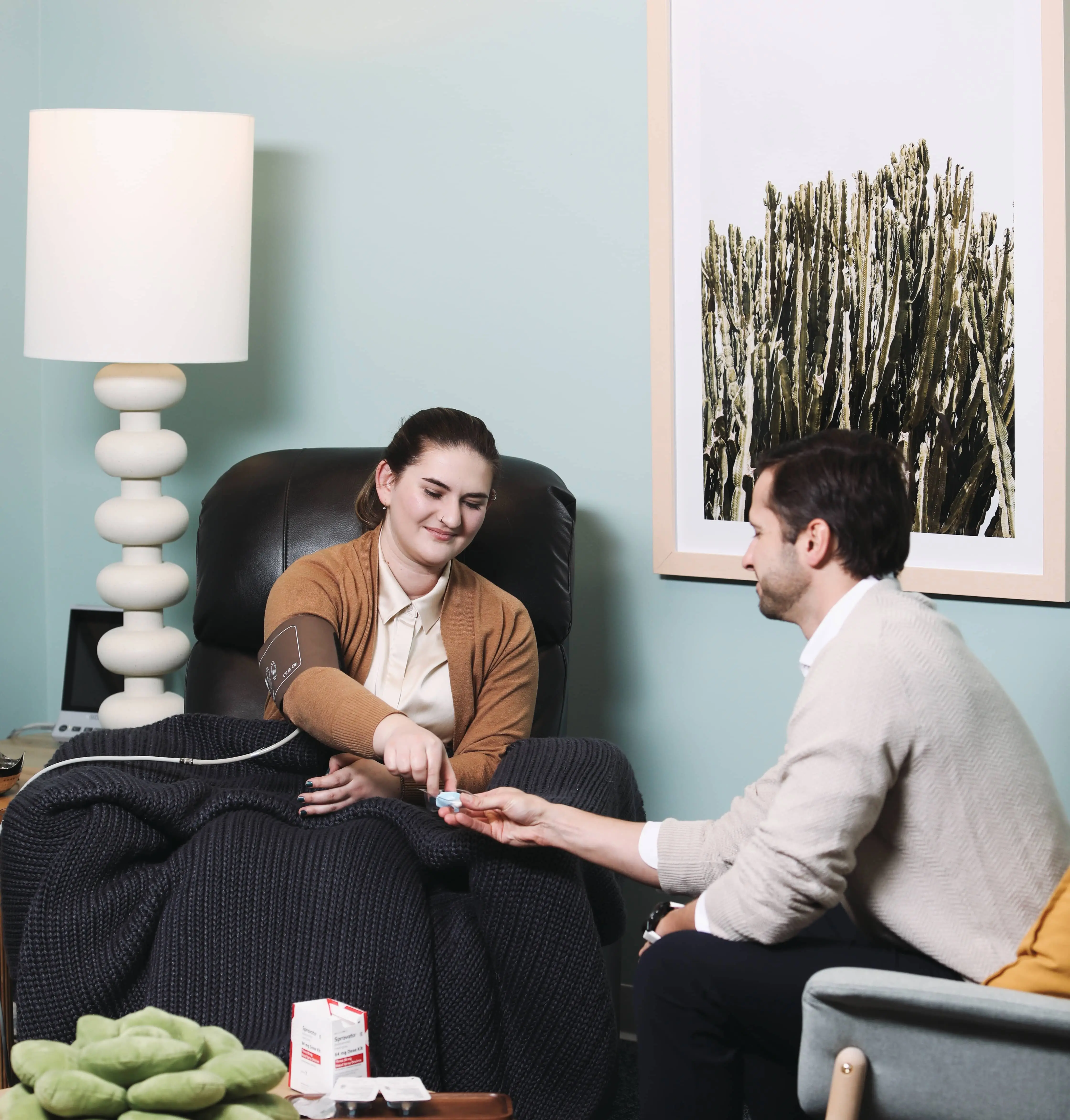 A smiling patient on a sofa receiving care from a provider in a calm, warm room